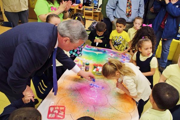 A happy Mayor Kenney helping a preschooler with a glittery art project.